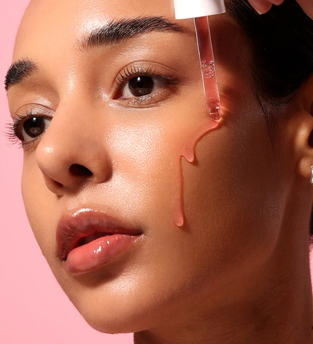 Close-up of a woman's face with a cosmetic product being applied to her skin against a pink background