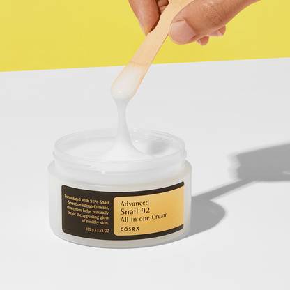 COSRX Advanced Snail 92 All in One Cream jar with a hand using a wooden spoon to scoop cream.