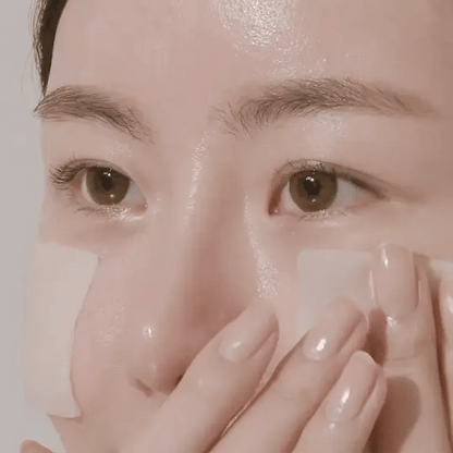 Close-up of a person applying cream to their face with a neutral background